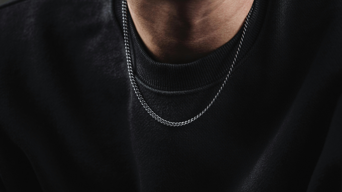 Close-up of a simple sterling silver necklace on a man’s neck over a black crewneck shirt, illustrating minimalist styling for daily wear in 2025.