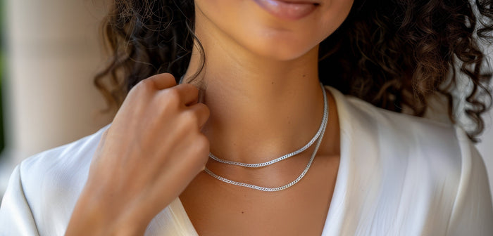 Woman wearing a layered silver chain necklace with a white blouse, showcasing a minimalist and elegant jewelry style.