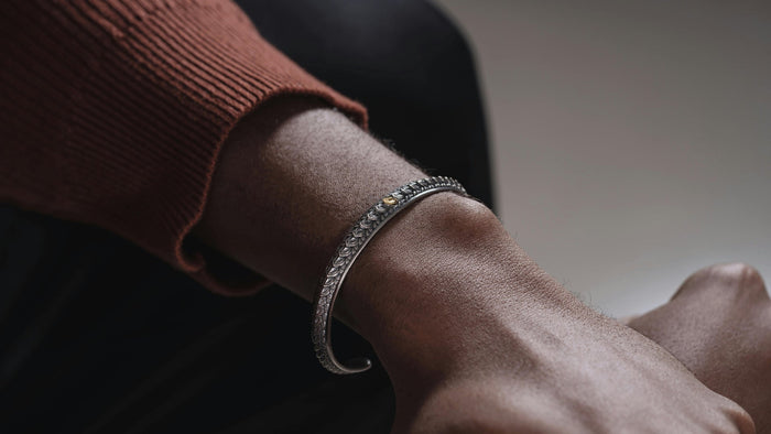 Close-up of a man wearing a detailed sterling silver cuff bracelet with a subtle gold accent.
