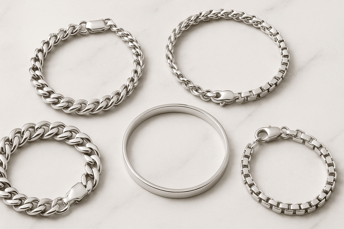 Flat-lay of five Italian 925 silver bracelets arranged on a white marble background, showcasing various chain styles including curb, box, and a sleek bangle.